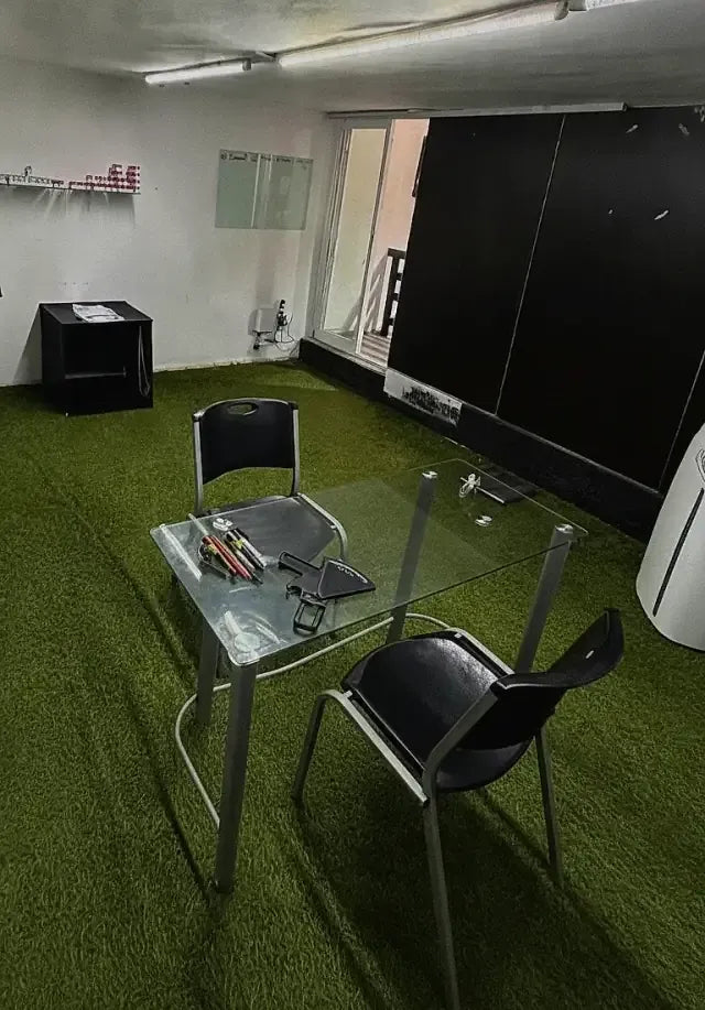 Consultorio de asesorías en el local Kong: mesa de vidrio y sillas sobre pasto sintético